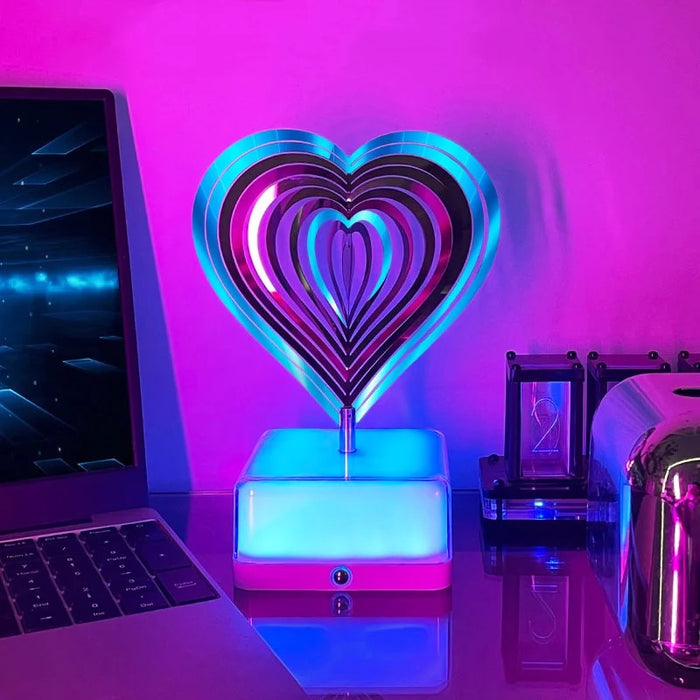 Love shape 3D Rotating Night Light placed next to a laptop on a table