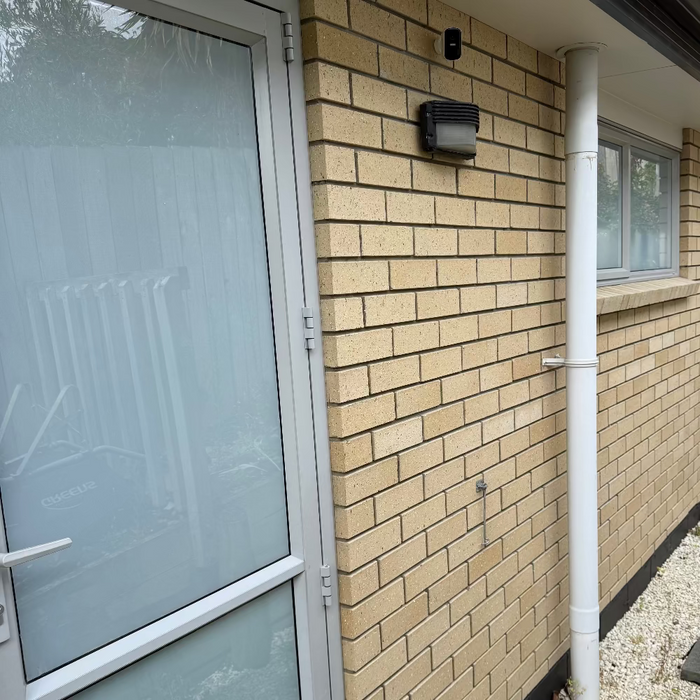 Beige brick wall with a frosted glass door and white pipe running vertically.