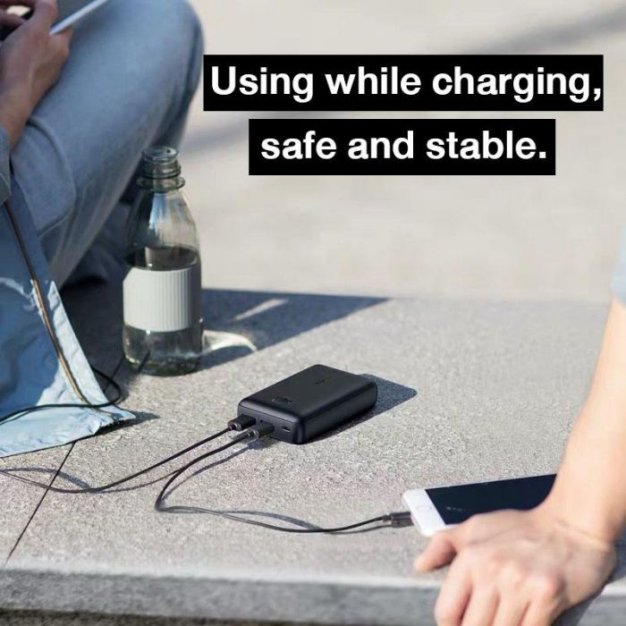Anker PowerCore Select 10000mAh Portable Power Bank placed on the floor next to a mobile phone, which is plugged into it