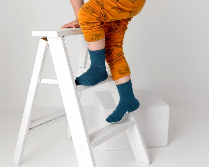Camden cotton crew socks: child standing on a chair in dark teal crew socks. Squid Socks, the brand seen on Shark Tank.