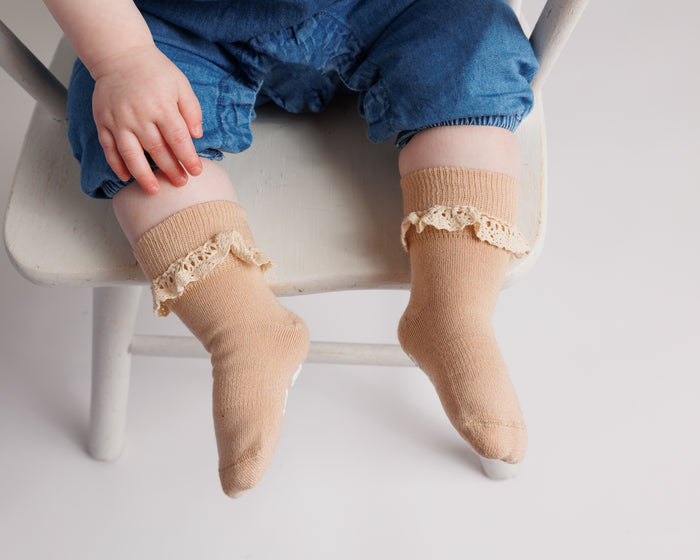 Candace kids socks: child seated on a chair wearing beige lace-trim socks. Squid Socks, the brand seen on Shark Tank.