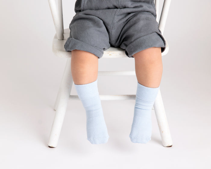 Casen kids socks: child seated on a chair wearing pale blue socks. Squid Socks, the brand seen on Shark Tank.
