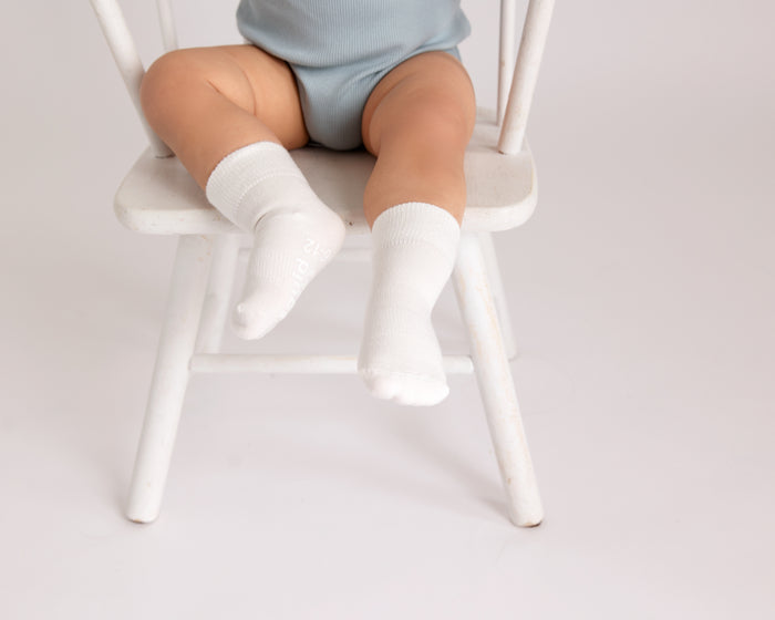 Casen kids socks: child seated on a chair wearing ivory socks. Squid Socks, the brand seen on Shark Tank.