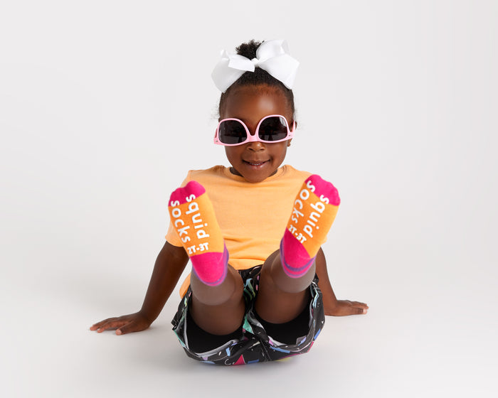 CeCe kids socks: child seated showing orange sock soles with pink toes. Squid Socks, the brand seen on Shark Tank.