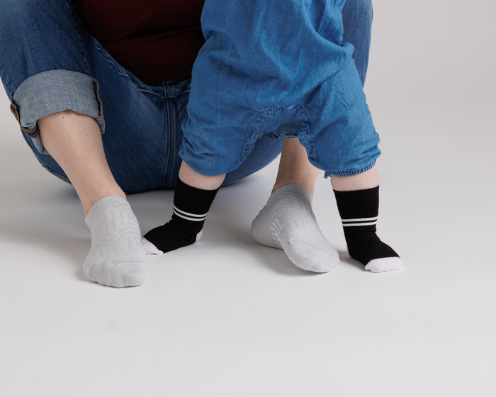 City kids socks: adult supporting a standing baby in black striped-cuff socks. Squid Socks, the brand seen on Shark Tank.