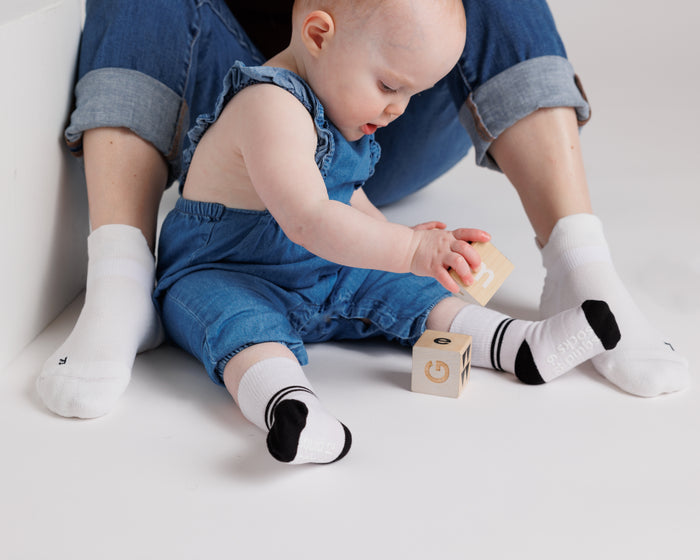 City kids socks: child seated playing with blocks in white striped-cuff socks. Squid Socks, the brand seen on Shark Tank.