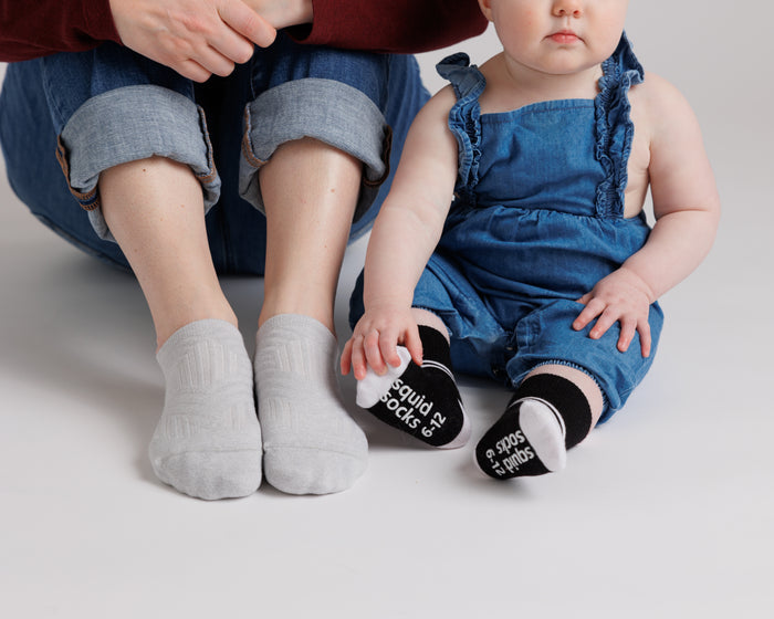 City kids socks: adult and child seated wearing gray and black socks. Squid Socks, the brand seen on Shark Tank.