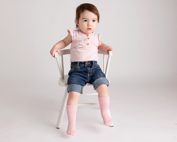 Claire kids socks: child seated on a chair wearing soft pink socks. Squid Socks, the brand seen on Shark Tank.