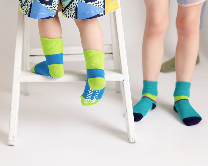 Clint kids socks: children wearing blue and teal color-block socks by a chair. Squid Socks, the brand seen on Shark Tank.