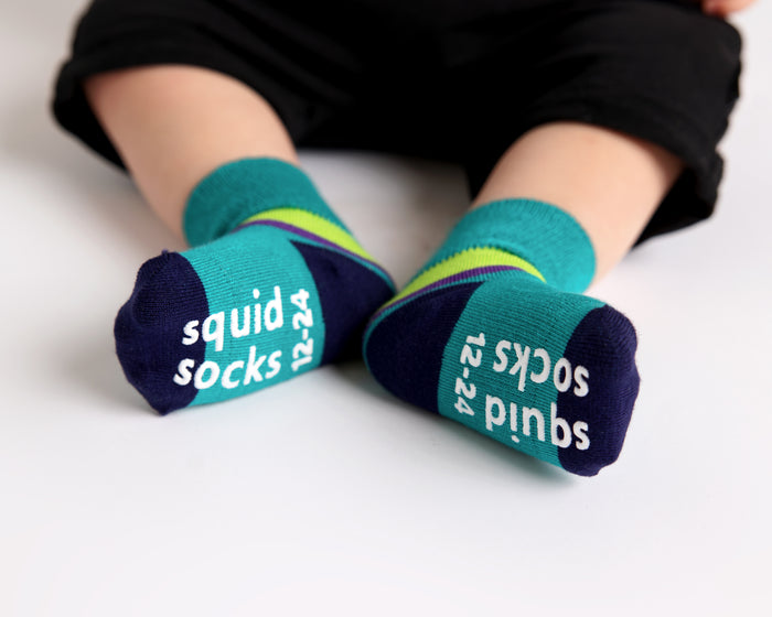 Clint kids socks: child seated showing teal sock soles. Squid Socks, the brand seen on Shark Tank.
