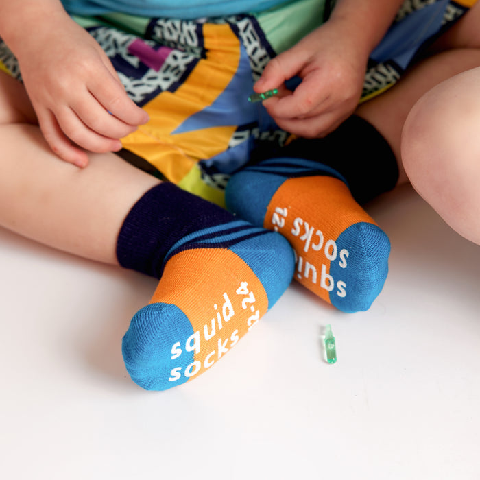 Clint kids socks: child seated showing orange sock soles. Squid Socks, the brand seen on Shark Tank.