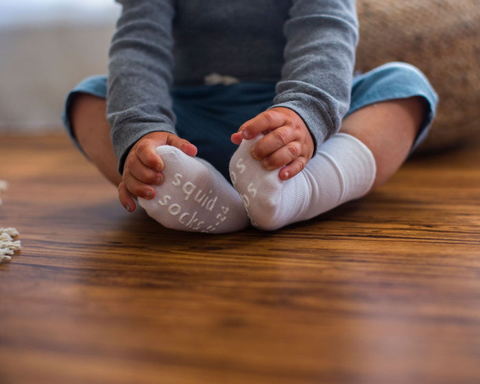 Cloud kids socks: child seated holding white socked feet. Squid Socks, the brand seen on Shark Tank.