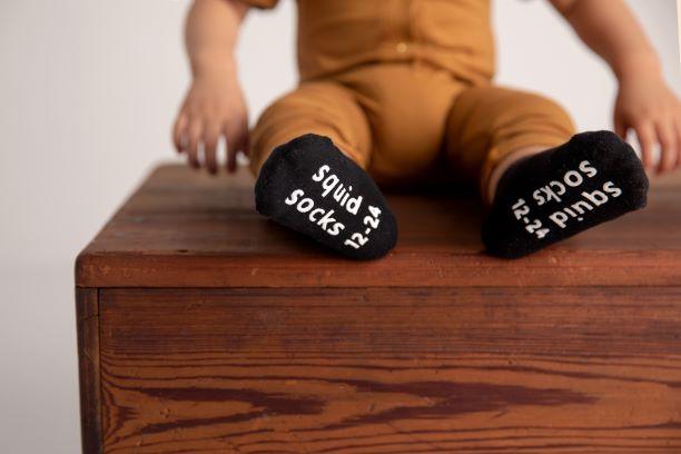 Coal kids socks: child seated showing black sock soles. Squid Socks, the brand seen on Shark Tank.