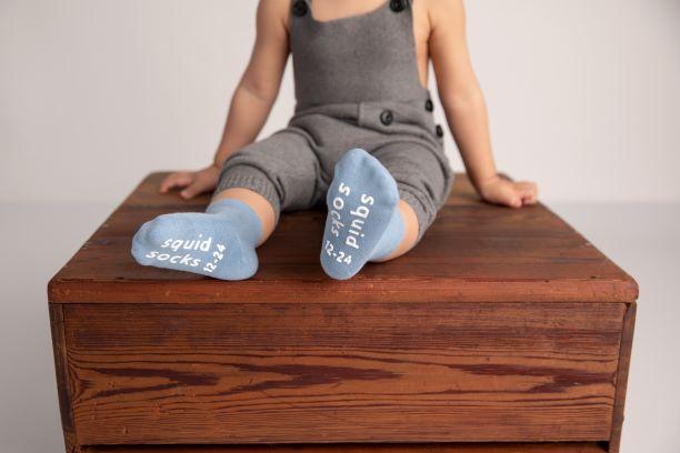 Colby kids socks: child seated with light blue sock soles facing forward. Squid Socks, the brand seen on Shark Tank.