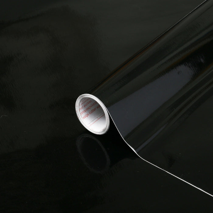 A roll of black glossy adhesive vinyl on a black glossy surface.