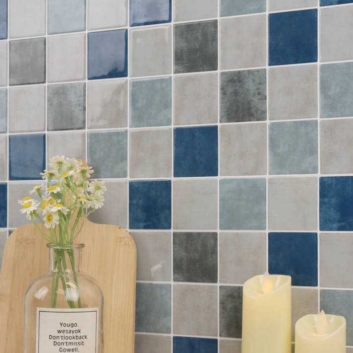 Decorative setting with a vase, croissant, and candles against a tiled checkered blue and grey wall.