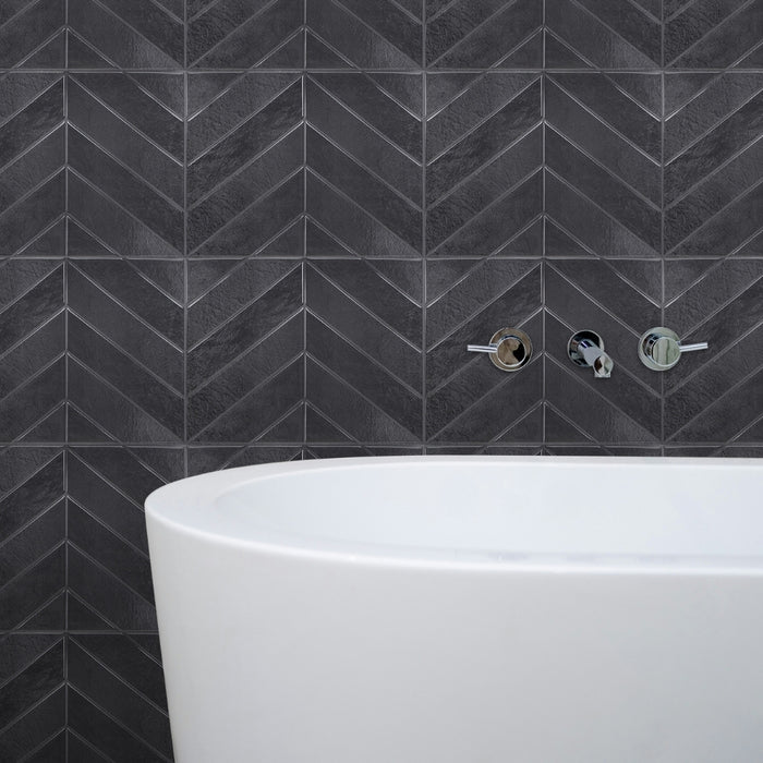Dark grey-black chevron-patterned tiles on a wall with a white bathtub below.