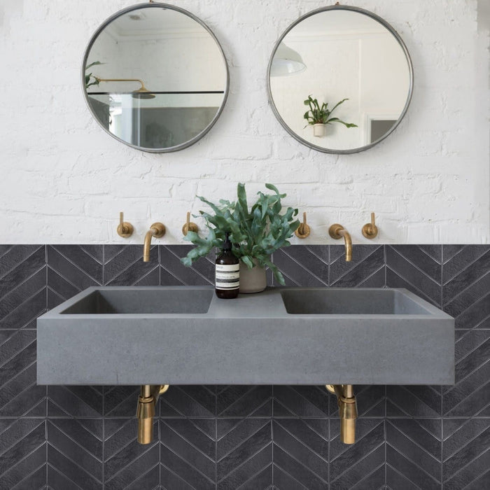 Bathroom with grey concrete sink, gold faucets, and round mirrors on a white brick and grey chevron wall.