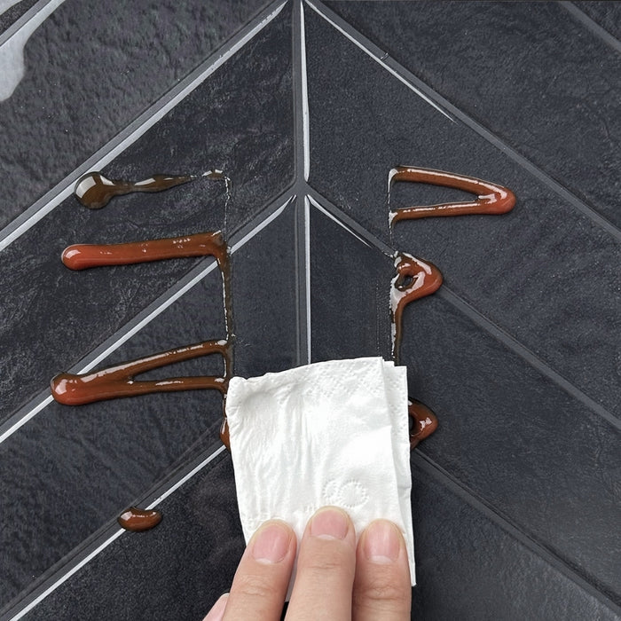 Hand using a paper towel to clean up sauce on a chevron tile.