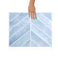 Hand holding a blue and white patterned peel and stick tile with a chevron design on a white background