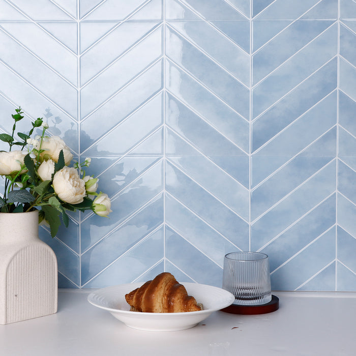 Blue chevron tiled wall with a plate of bread and a vase of flowers on a white surface.