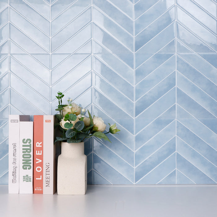 Blue chevron patterned tiles on a wall with books and a vase in the foreground.