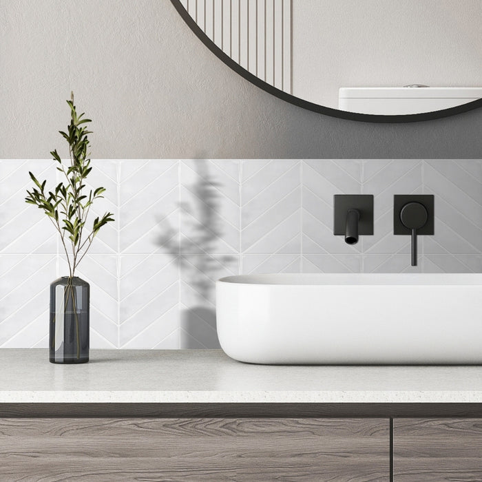 Modern bathroom with a white sinkand off white chevron tiles, black fixtures, and a vase with greenery.