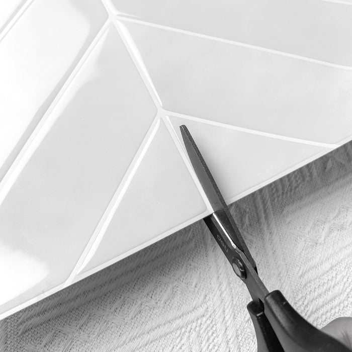 Scissors cutting a chevron off white tile
