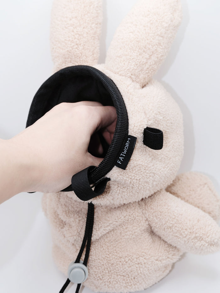 Handmade cream-colored Milk Tea Bunny plush climbing chalk bag with long floppy ears. Cute bouldering gift featuring a reinforced 12cm rim, secure drawstring, and deep black fleece lining. High-performance bouldering gear by Fatworm.