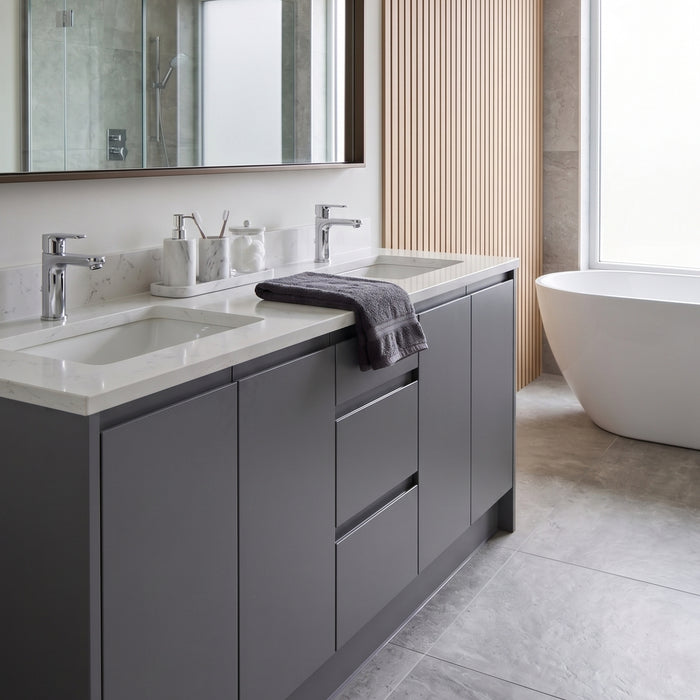 A modern bathroom vanity with a textured satin dark grey vinyl wrapped cabinet, a white double sink countertop, chrome faucets, and a folded dark grey towel, shown in a styled bathroom next to a freestanding bathtub.