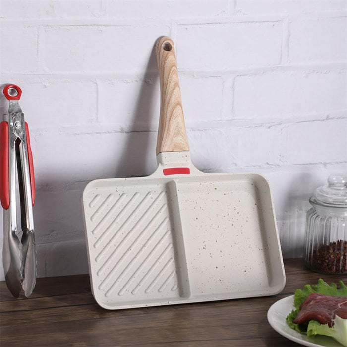 White frying pan with wooden handle on a wooden surface with a white brick wall background.