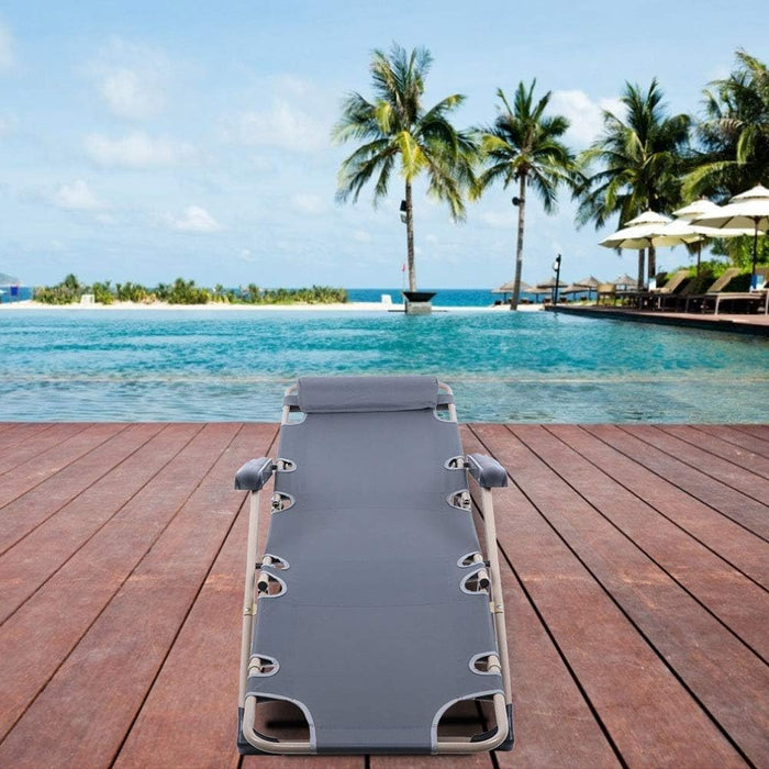 Gray lounge chair on a wooden deck by a pool with palm trees and clear blue sky.