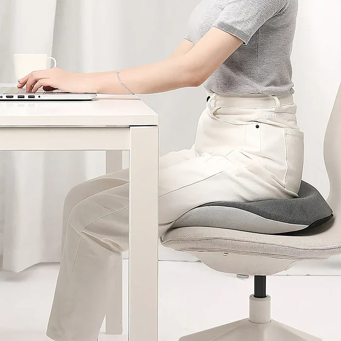 A person sitting at a desk using the Green Lion ErgoFlex Comfort Seat Cushion for ergonomic posture support and comfort.