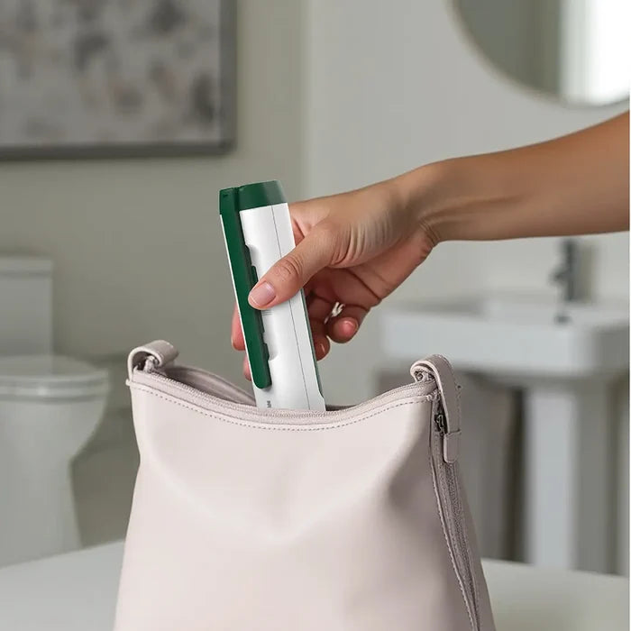 Hand placing a Green Lion Outlander Portable Bidetin to a beige bag in a bathroom setting.