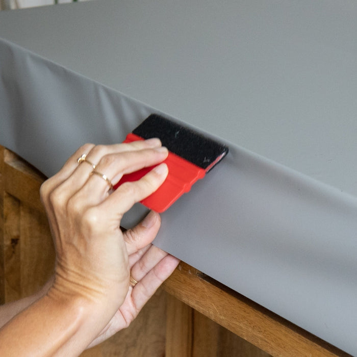 Close up of hands installing grey matte adhesive vinyl with a red squeegee.