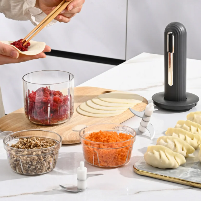 USB rechargeable food processor blender shown on a kitchen counter with detachable blades, glass bowls filled with minced meat, chopped mushrooms, and grated carrots, alongside dumpling wrappers and freshly made dumplings.