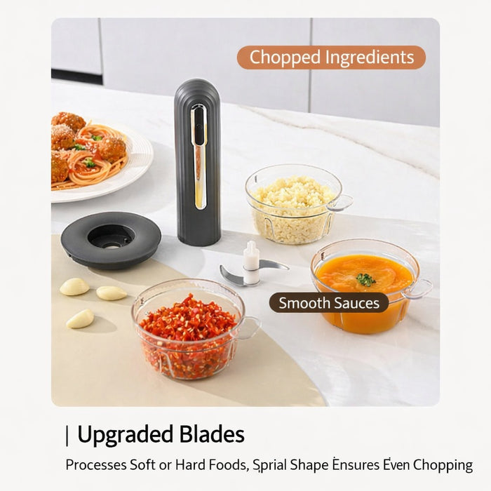 USB rechargeable food processor blender being used to chop meat in a clear container on a kitchen counter, surrounded by chopped vegetables, mashed potatoes, and a plate of spaghetti with meatballs