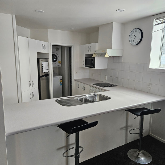 Modern kitchen with white cabinets, black bar stools, and a clock on the wall.