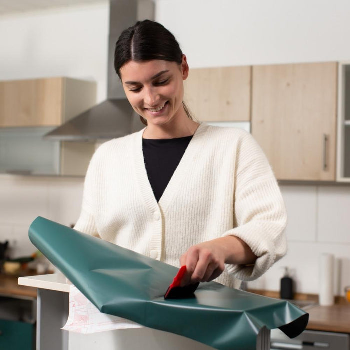 A lady installing mallard green matte adhesive vinyl onto a kitchen drawer.