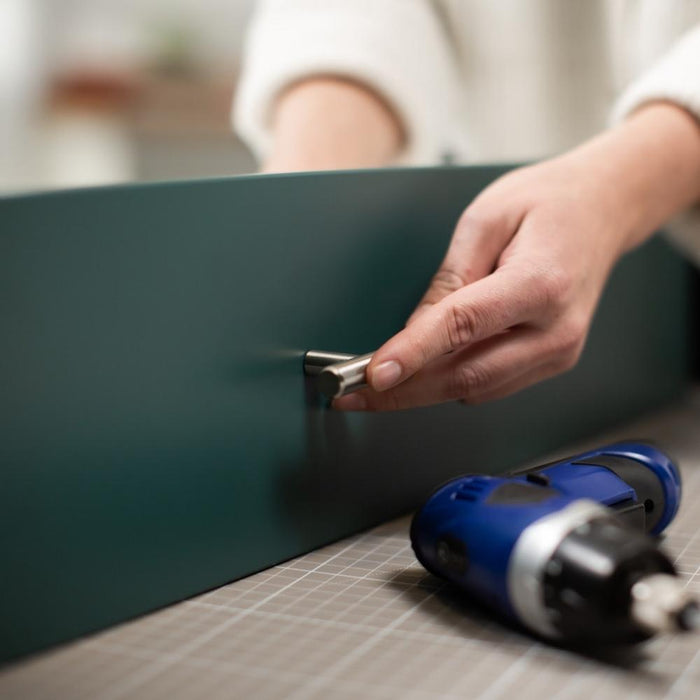 A hand attaching a drawer handle onto a mallard green matte vinyl wrapped drawer.