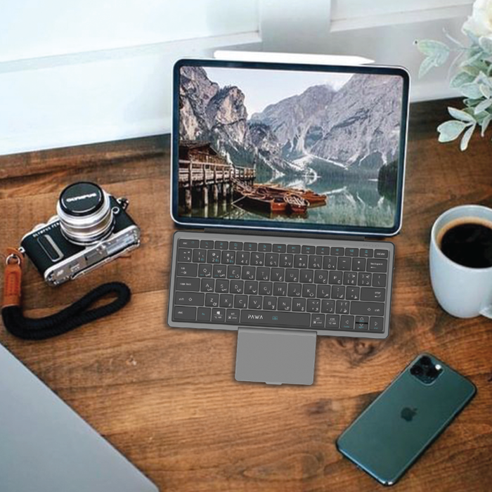 Tablet with PAWA Tri-Fold Wireless Bluetooth Keyboard on a wooden desk with camera, phone, and coffee cup.