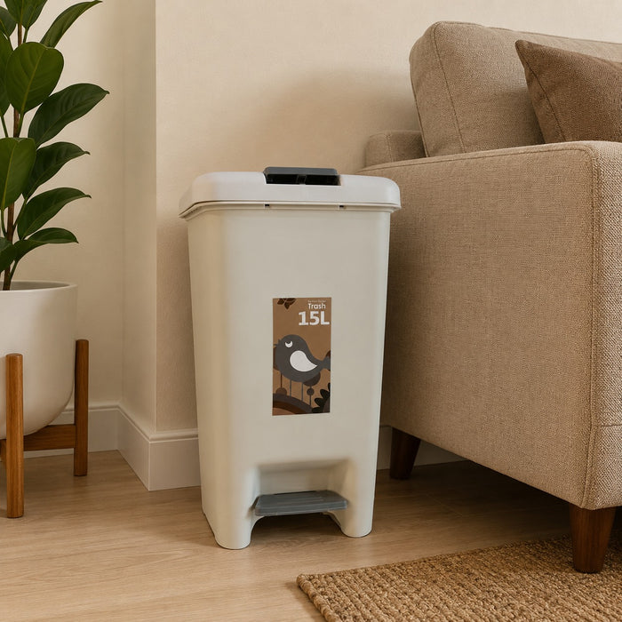 A 15L plastic trash can with a foot pedal and a hinged lid, shown in a home setting next to a beige sofa and a potted plant.