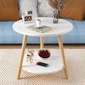Round white coffee table with wooden legs, holding a cup, book, photo frame, and decor; cherries and a game controller below in a living room