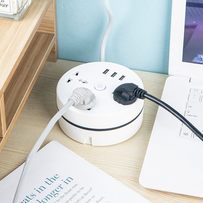 Round Universal Converter Power Strip Adapter - Extension Socket 3 Outlets with 3 USB Ports placed on desk next to a laptop  which is plugged into the power strip