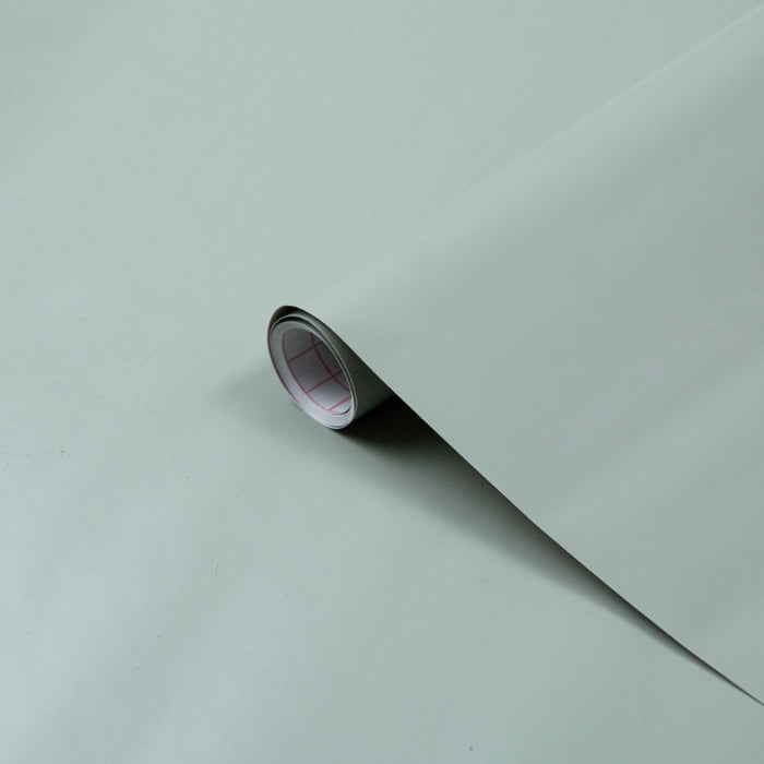 A rolled up piece of sage green matte adhesive vinyl with one end slightly lifted, showing the matte finish.