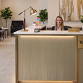 Receptionist at a Satin Bronze Metallic vinyl wrapped hotel desk with a 'Reception' sign, plants, and a lamp.