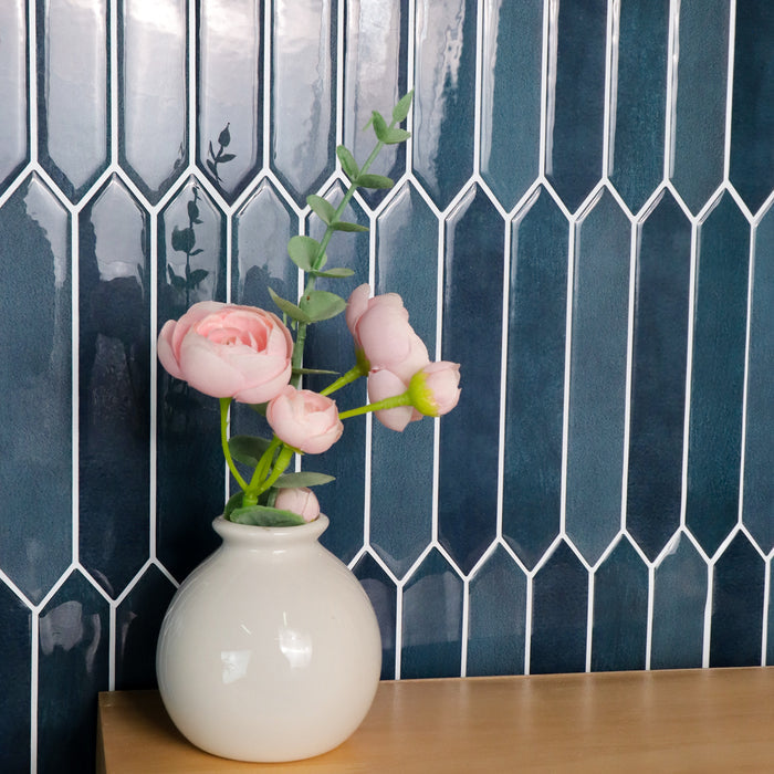 White vase with pink flowers against a blue tiled wall