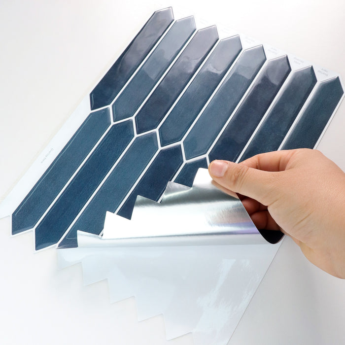 Hand applying a geometric patterned picket blue peel and stick tiles to a surface