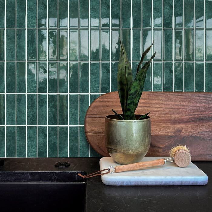 Emerald green stacked subway tiles on a wall behind a kitchen benchtop with a wooden cutting board and a plant.