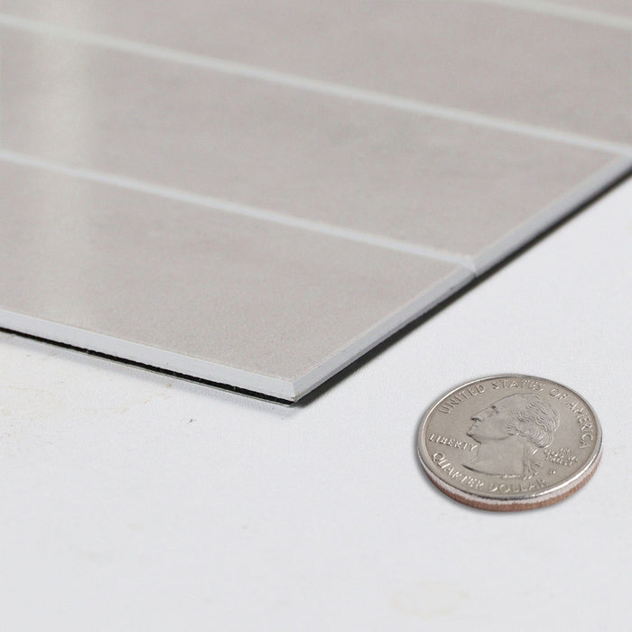 A close-up of a light pink rectangular panel with a brushed metallic finish, shown on a white surface next to a U.S. coin